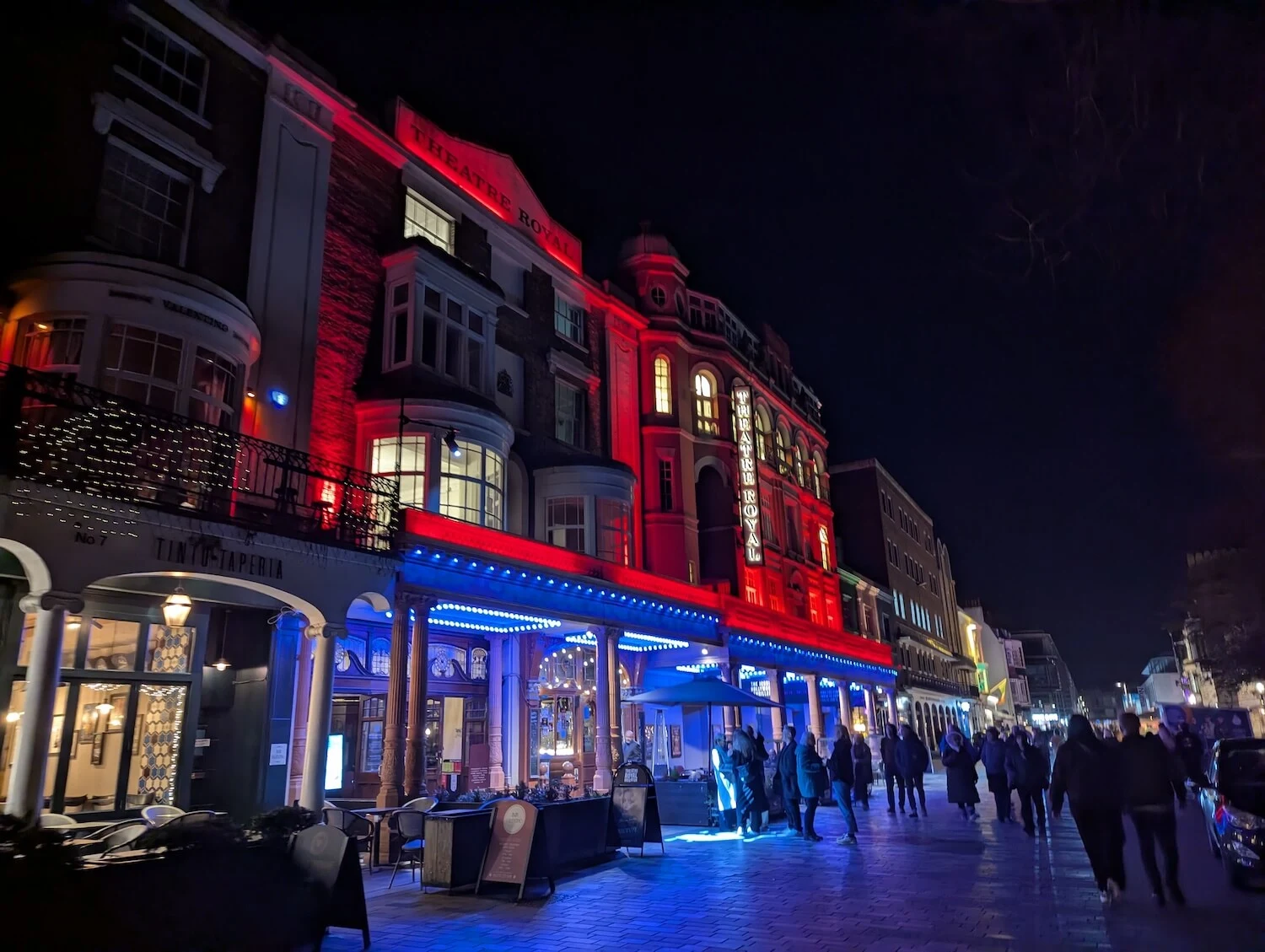 Buildings on a street in Brighton lit up by red and blue lights.