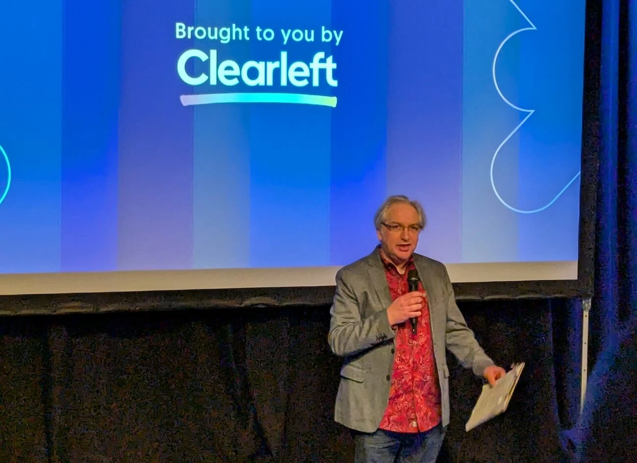 A man standing in front of a large projector screen with the text 'brought to you by clearleft'